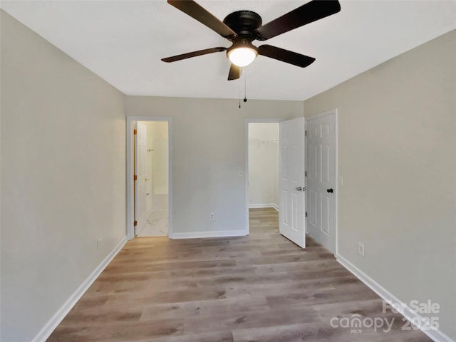 unfurnished bedroom featuring ensuite bath, a spacious closet, light hardwood / wood-style flooring, a closet, and ceiling fan