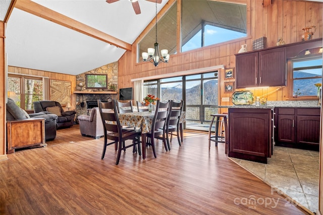 dining space featuring beam ceiling, a stone fireplace, light hardwood / wood-style flooring, and wooden walls