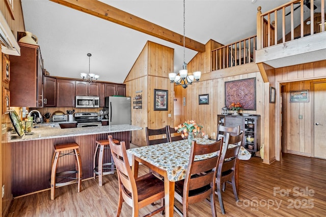 dining space with beamed ceiling, wood walls, sink, and a notable chandelier