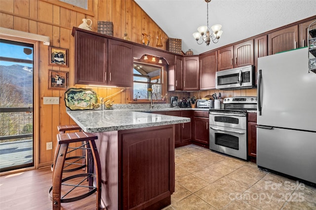 kitchen featuring a breakfast bar, decorative light fixtures, lofted ceiling, stainless steel appliances, and light stone countertops