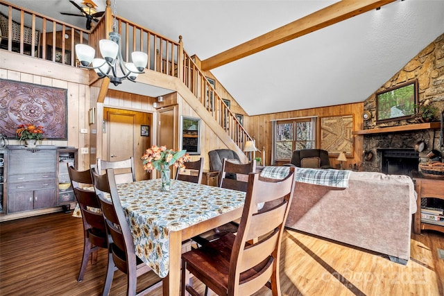 dining room with a stone fireplace, dark hardwood / wood-style floors, wooden walls, a chandelier, and beam ceiling