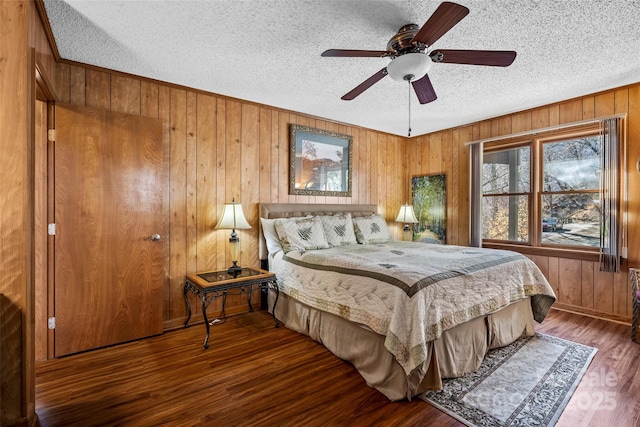 bedroom with ceiling fan, wooden walls, a textured ceiling, and dark hardwood / wood-style flooring