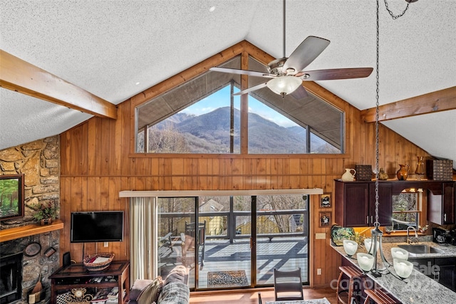 living room featuring wood walls, a stone fireplace, sink, and vaulted ceiling with beams