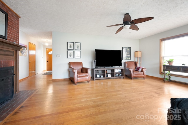 living room featuring a ceiling fan, light wood-type flooring, a fireplace, and a textured ceiling