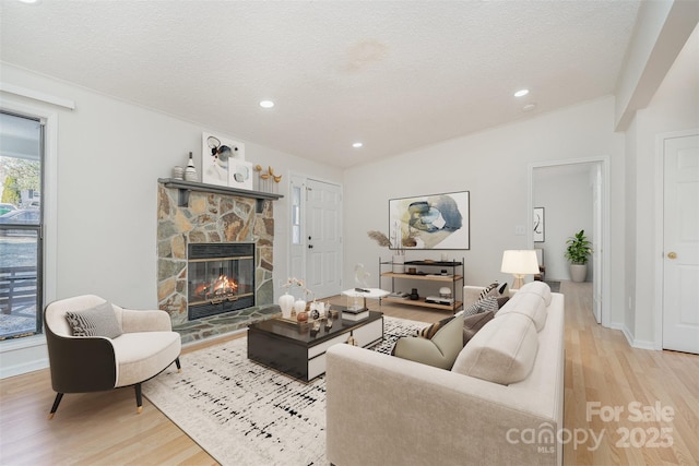 living room with lofted ceiling, a stone fireplace, a textured ceiling, and light wood-type flooring