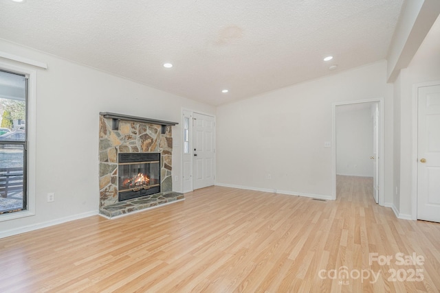 unfurnished living room featuring a stone fireplace, a textured ceiling, and light wood-type flooring