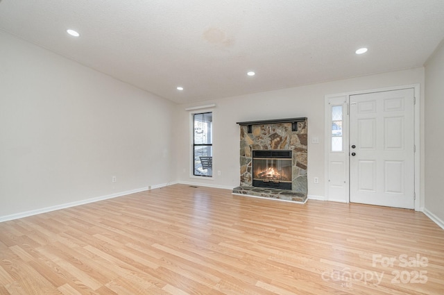 unfurnished living room with a stone fireplace, light hardwood / wood-style flooring, and a textured ceiling