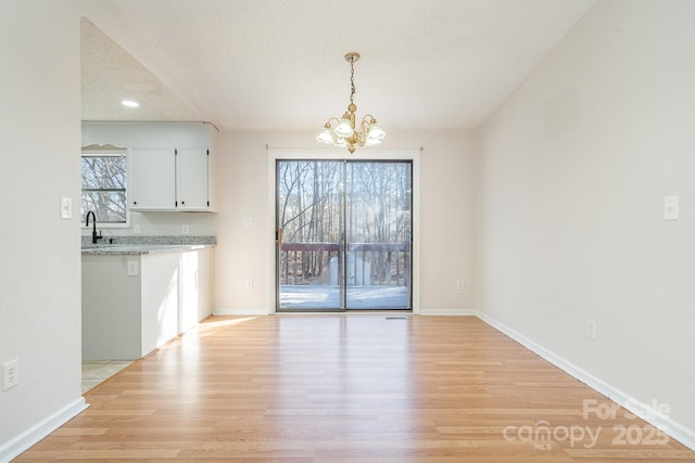 unfurnished dining area featuring sink, an inviting chandelier, a textured ceiling, and light hardwood / wood-style flooring