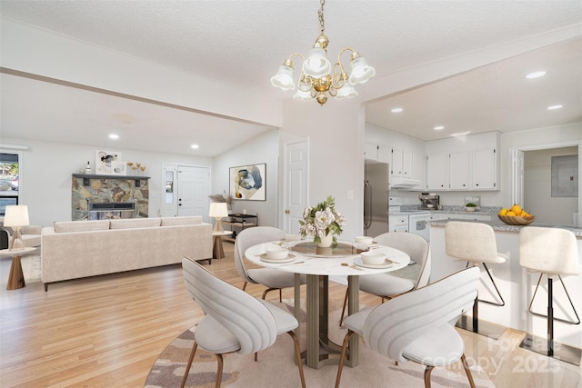 dining space with a notable chandelier, a stone fireplace, light hardwood / wood-style floors, and a textured ceiling