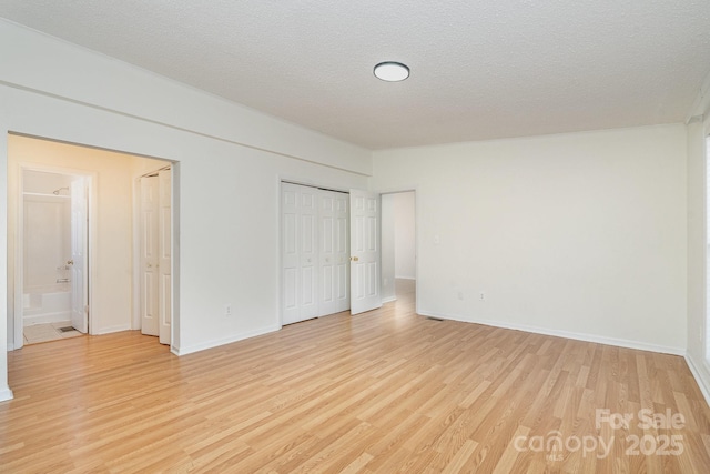 unfurnished bedroom featuring ensuite bathroom, a textured ceiling, and light wood-type flooring