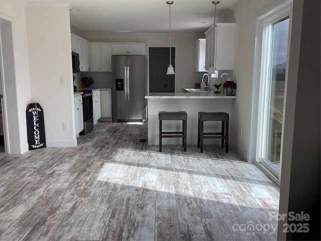 kitchen featuring hardwood / wood-style floors, white cabinetry, crown molding, stainless steel appliances, and kitchen peninsula