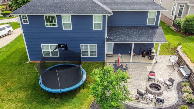 137 Tenth Green Ct, Statesville, NC 28677 - rear view of house with an outdoor fire pit, a trampoline, a shingled roof, a patio area, and a lawn
