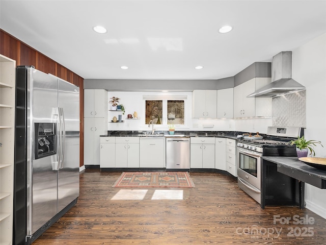 kitchen with dark countertops, stainless steel appliances, wall chimney range hood, open shelves, and a sink