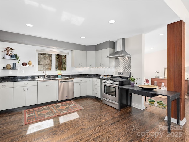 kitchen featuring a sink, appliances with stainless steel finishes, wall chimney range hood, dark countertops, and dark wood finished floors