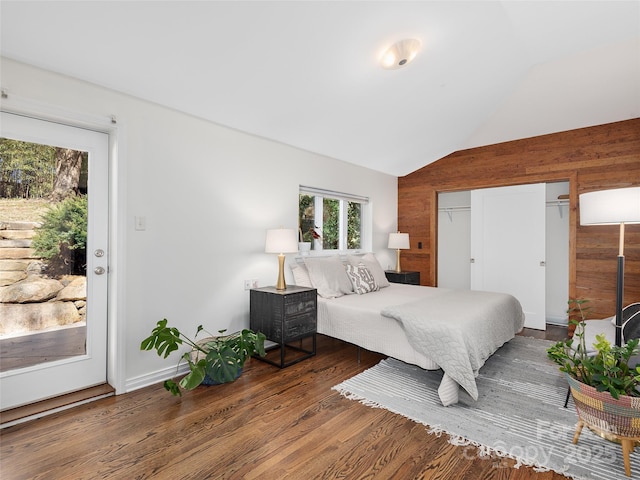 bedroom with lofted ceiling, a closet, wood walls, and wood finished floors