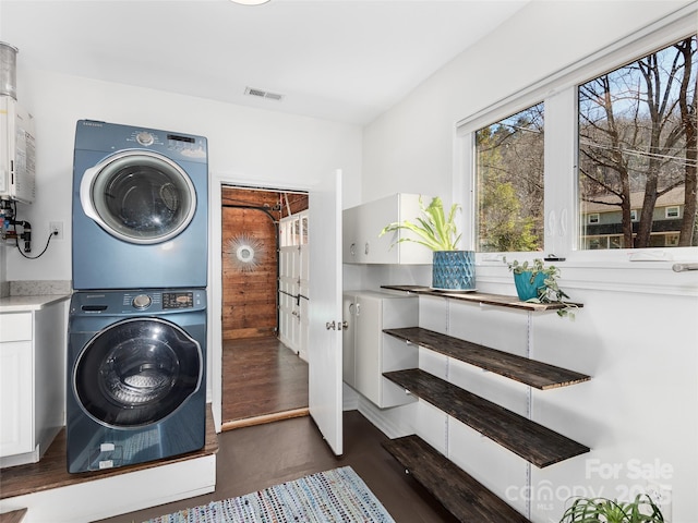 laundry area with cabinet space, visible vents, and stacked washing maching and dryer