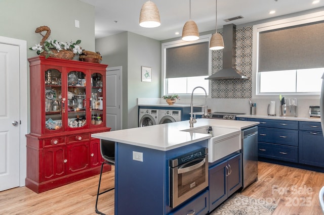 kitchen featuring wall chimney exhaust hood, a kitchen bar, appliances with stainless steel finishes, an island with sink, and pendant lighting