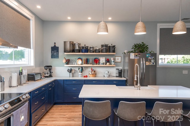 kitchen featuring stainless steel appliances, hanging light fixtures, blue cabinetry, and a kitchen breakfast bar