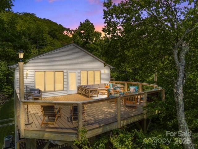 back of house at dusk with a wooden deck and an outdoor hangout area