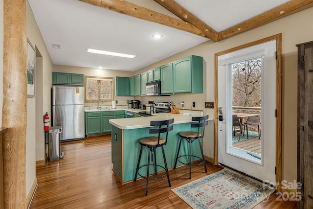 kitchen featuring stainless steel appliances, a peninsula, light countertops, dark wood-style floors, and beamed ceiling