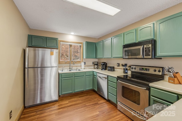 kitchen with a sink, light wood-style floors, green cabinets, light countertops, and appliances with stainless steel finishes