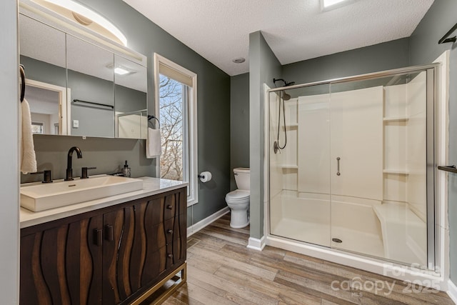 full bath with toilet, wood finished floors, a textured ceiling, vanity, and a shower stall