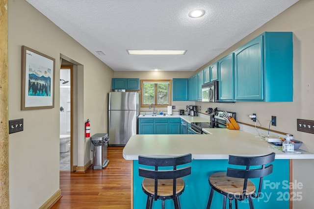 114 Spruce Hollow Rd, Beech Mountain, NC 28604 - kitchen featuring stainless steel appliances, blue cabinets, light wood-style flooring, a textured ceiling, and a peninsula
