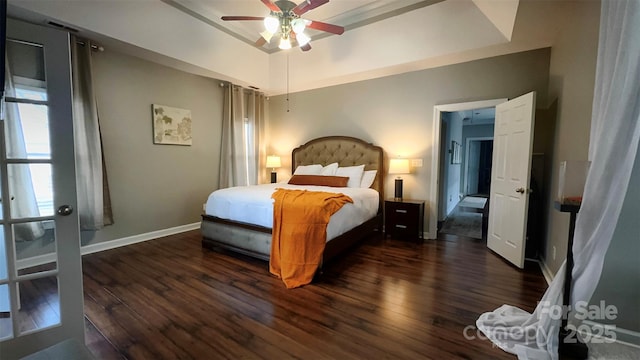 bedroom with ceiling fan, a tray ceiling, and dark hardwood / wood-style flooring