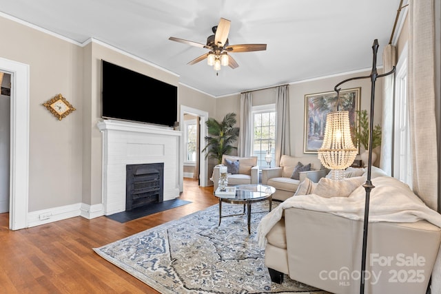 living room featuring hardwood / wood-style flooring, ceiling fan, ornamental molding, and a fireplace