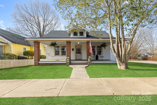 view of front facade featuring covered porch, roof with shingles, fence, and a front yard
