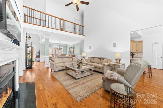 living room with ornate columns, ornamental molding, ceiling fan with notable chandelier, and light hardwood / wood-style flooring