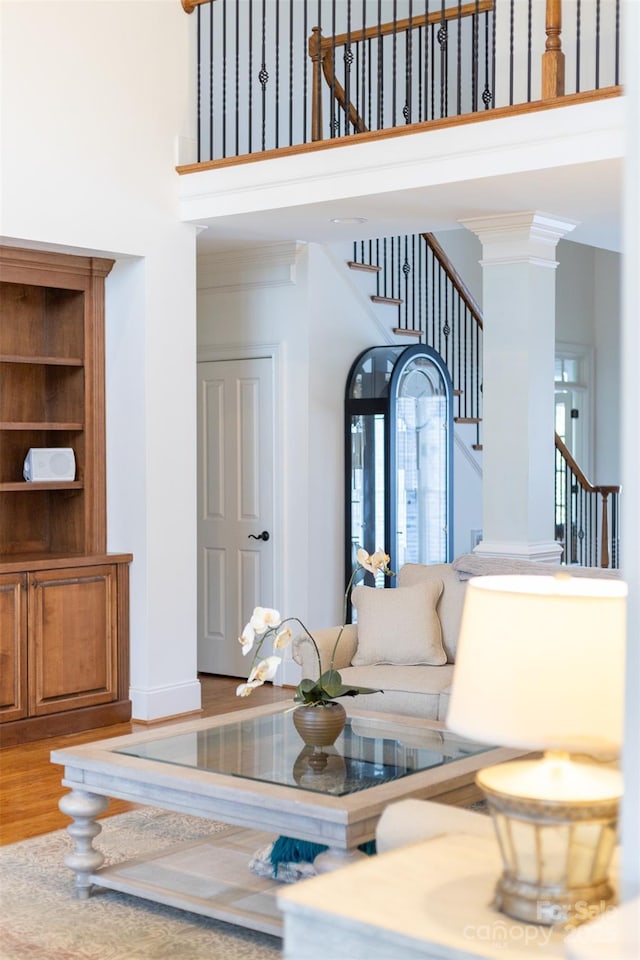 living room featuring ornate columns, ornamental molding, hardwood / wood-style floors, and a high ceiling