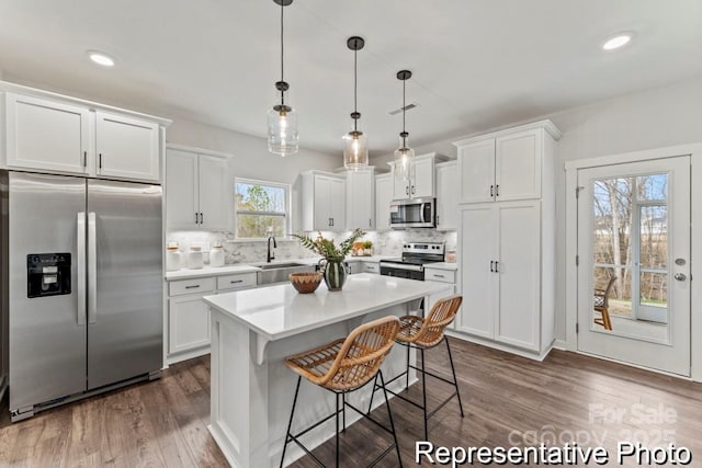 kitchen featuring appliances with stainless steel finishes, hanging light fixtures, a center island, white cabinets, and dark hardwood / wood-style flooring