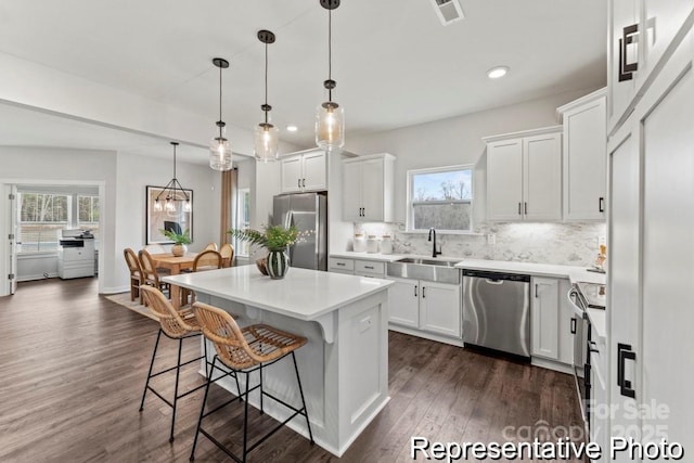 kitchen with sink, appliances with stainless steel finishes, white cabinetry, a kitchen island, and decorative light fixtures