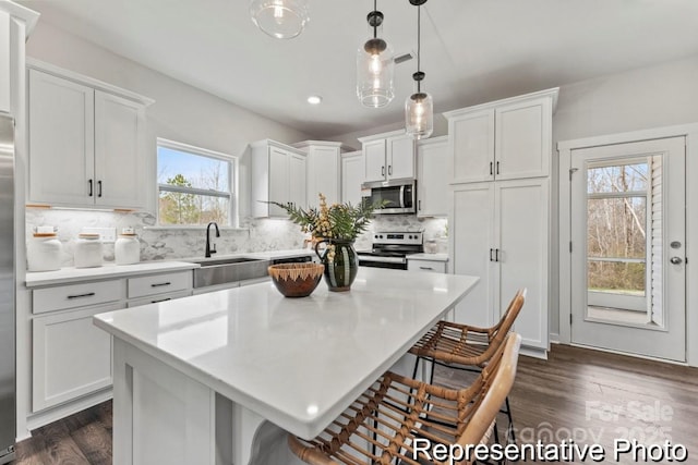 kitchen with sink, white cabinetry, appliances with stainless steel finishes, a kitchen island, and pendant lighting