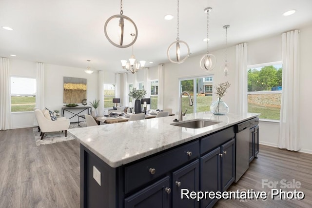 kitchen with light stone counters, a sink, dishwasher, a kitchen island with sink, and wood finished floors
