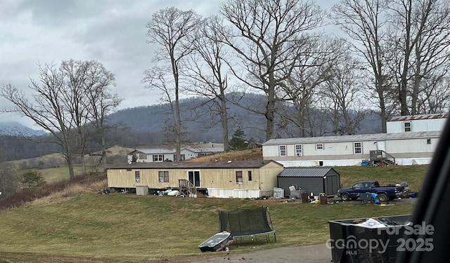 back of property featuring a trampoline, an outbuilding, a yard, a mountain view, and a shed