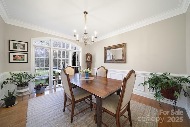 dining room featuring a chandelier, a wainscoted wall, wood finished floors, and crown molding