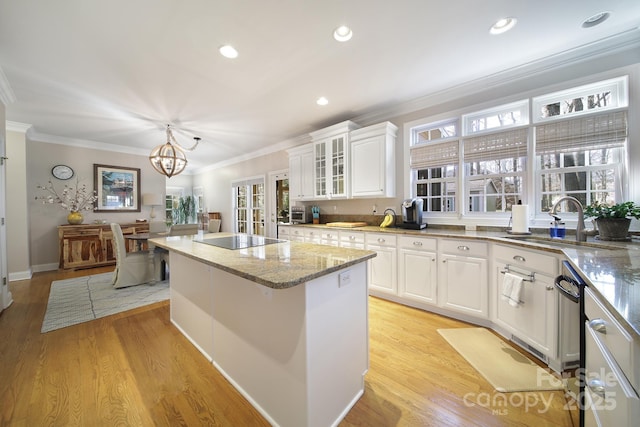 kitchen with crown molding, black electric stovetop, light wood-style flooring, a sink, and a kitchen island