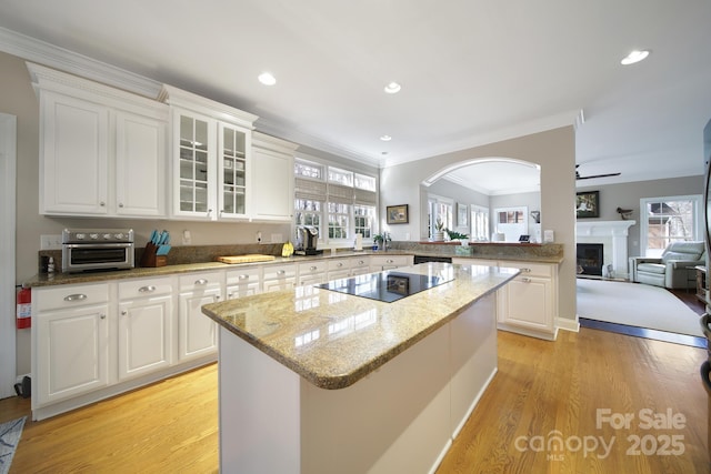 kitchen featuring light wood-style flooring, a kitchen island, glass insert cabinets, light stone countertops, and black electric cooktop