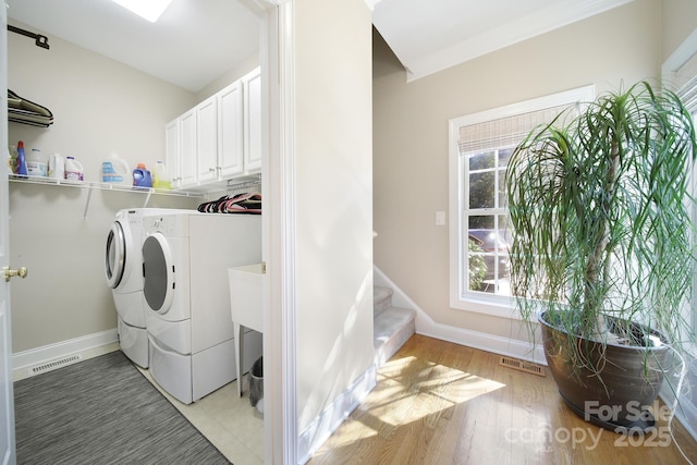 laundry area with light wood-style floors, baseboards, visible vents, and washer and dryer