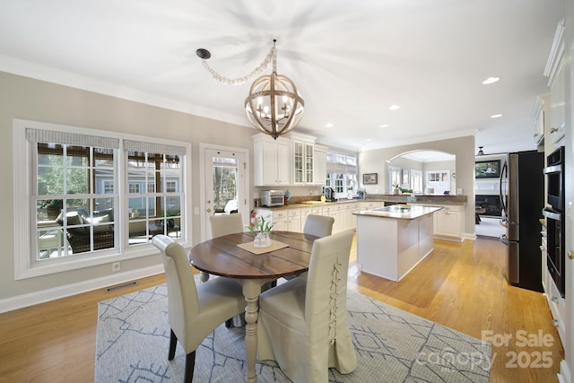 dining area with light wood-type flooring, visible vents, and crown molding