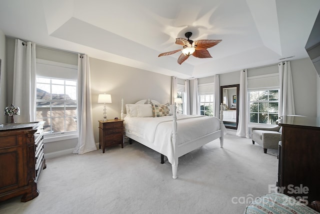 bedroom featuring baseboards, a tray ceiling, a ceiling fan, and light colored carpet