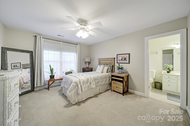 bedroom with ceiling fan, ensuite bathroom, light carpet, visible vents, and baseboards