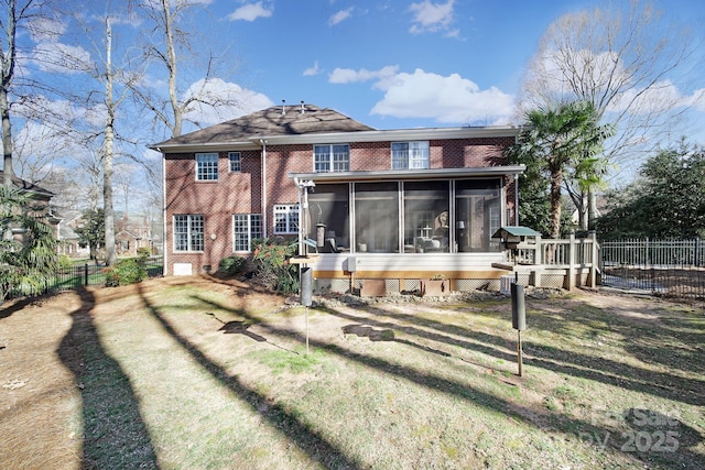 rear view of house featuring brick siding, a lawn, fence, and a sunroom