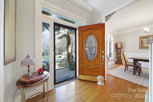 foyer with ornamental molding, light wood-style flooring, and a notable chandelier