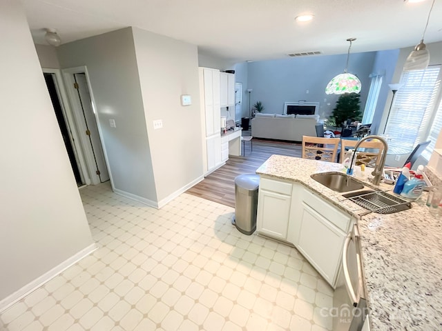 kitchen featuring pendant lighting, sink, white cabinets, stainless steel dishwasher, and light stone countertops