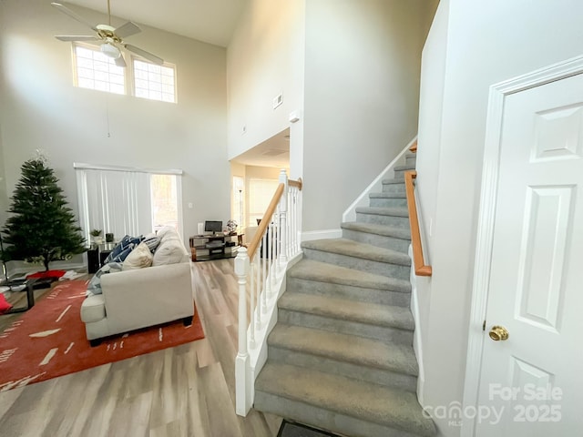 staircase with hardwood / wood-style flooring, a high ceiling, a healthy amount of sunlight, and ceiling fan