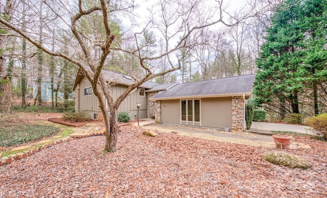 rear view of property featuring stone siding and roof with shingles