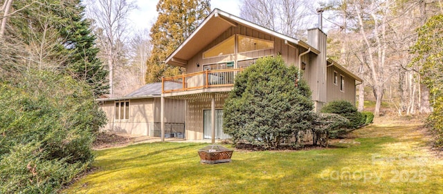 back of house with an outdoor fire pit, a chimney, and a lawn